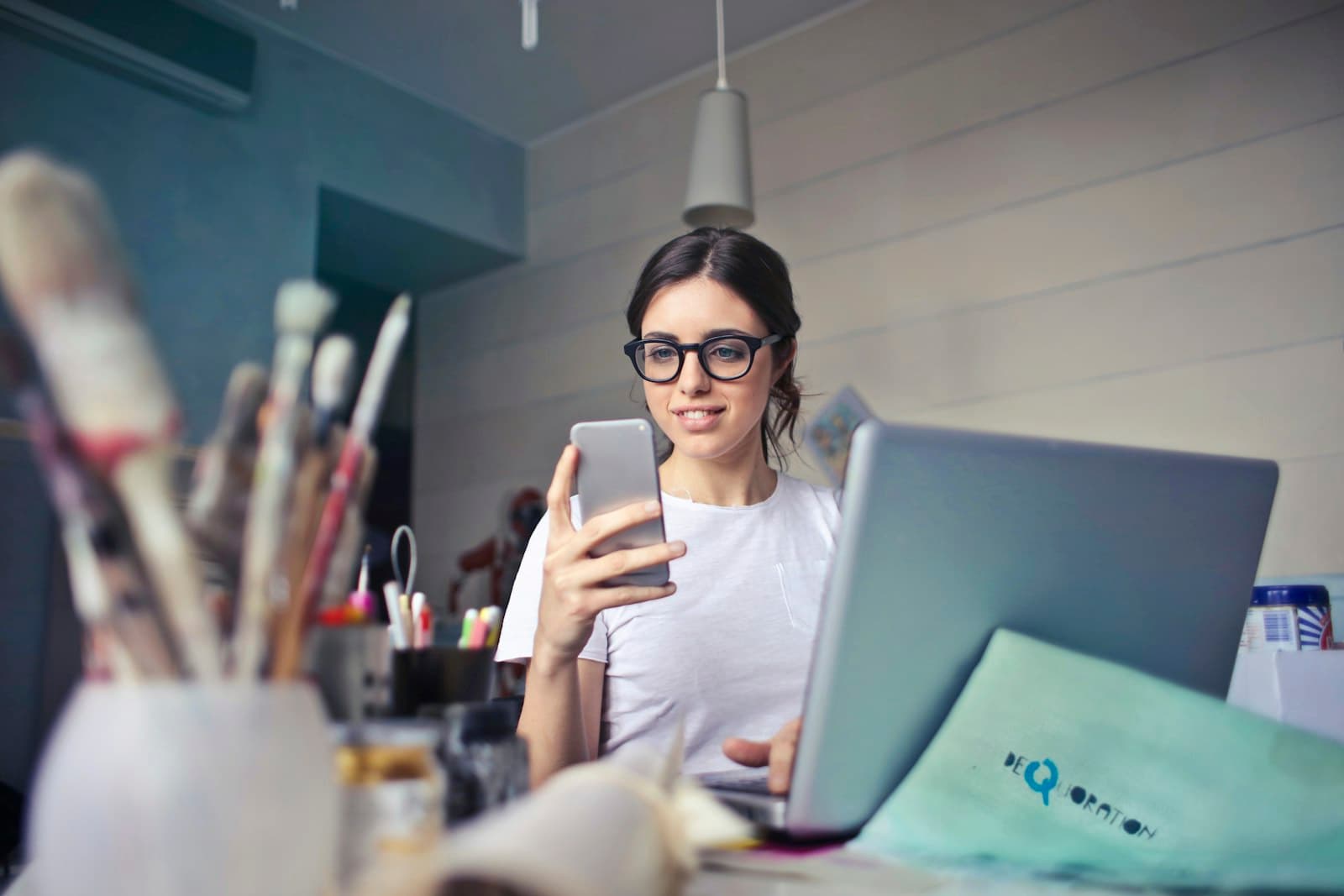 A small business owner checks her phone at her workspace, laptop open.